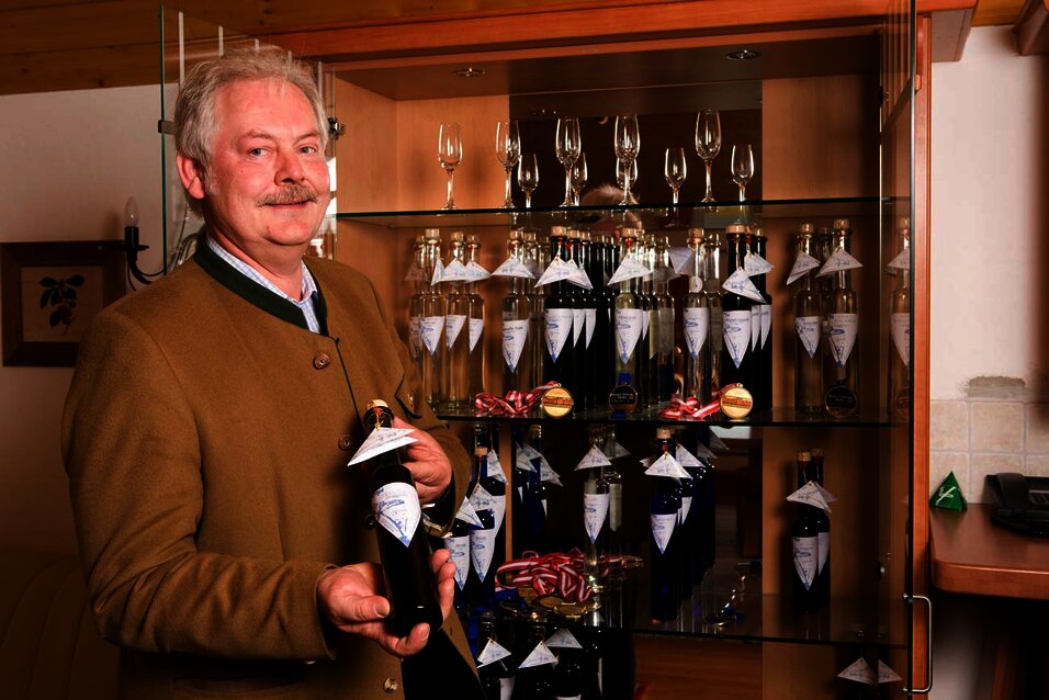 Karl Langmayr mit einer Flasche Edelbrand vor einer Vitrine mit mehreren Flaschen