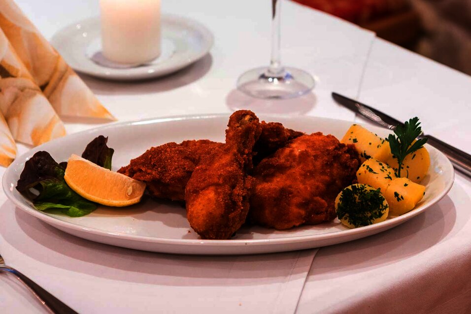 Backhendl mit Kartoffeln und einer Zitrone, garniert auf einem weißen Teller