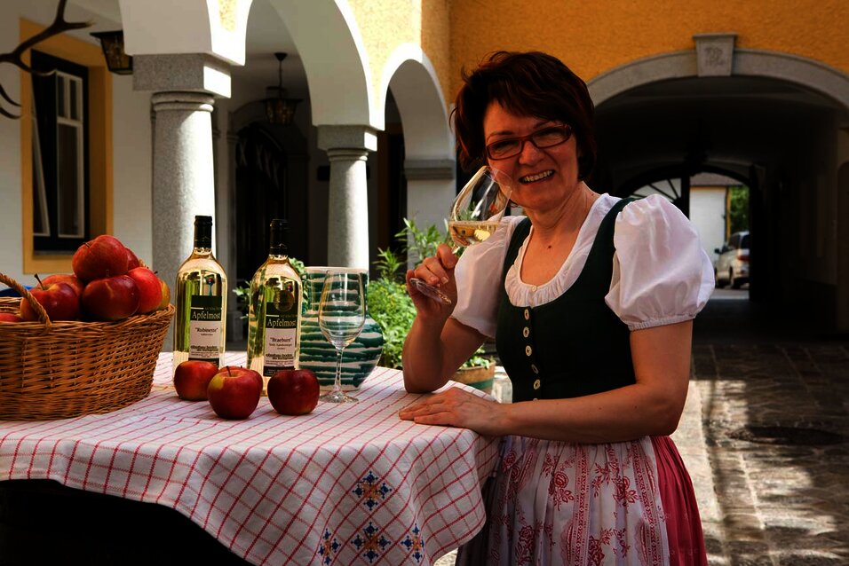 Paula Langmayr in einem Dirndl mit einem Glas Most an einem Stehtisch mit Tischtuch