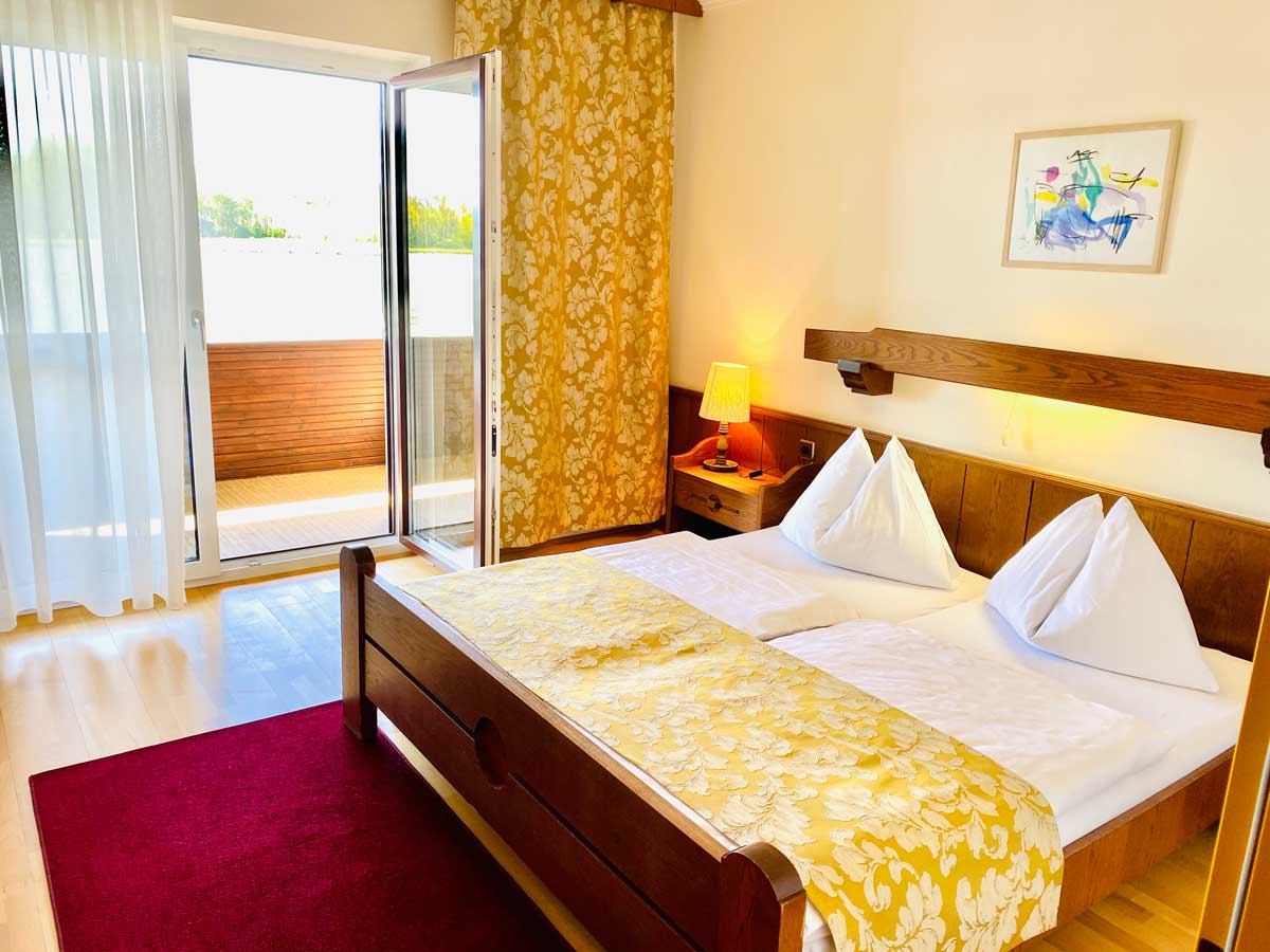 Hotelzimmer mit einem Doppelbett in weiß und gelber Decke, Blick auf die geöffnete Balkontür